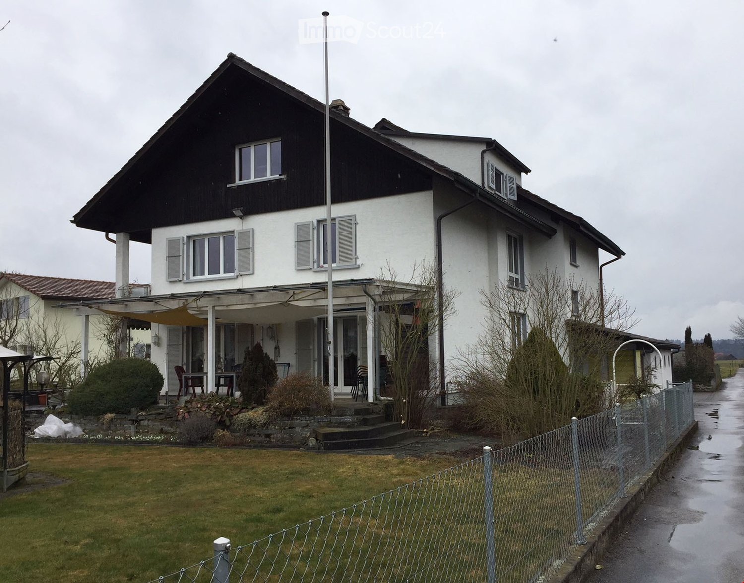 Two-story house with white walls, black roof, multiple windows, and a covered porch area with outdoor furniture.