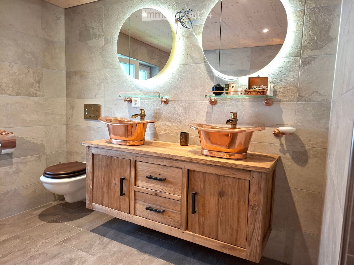 Elegant bathroom with two copper sinks, wooden vanity, large round mirrors, and a toilet.