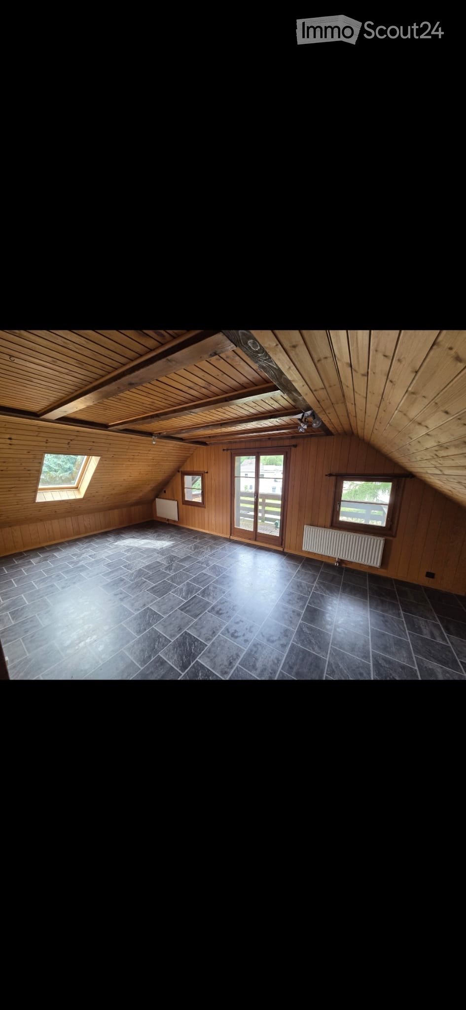 Empty attic space with wooden walls and ceiling, dark tiled floor, skylight windows, and a sliding glass door leading outside.