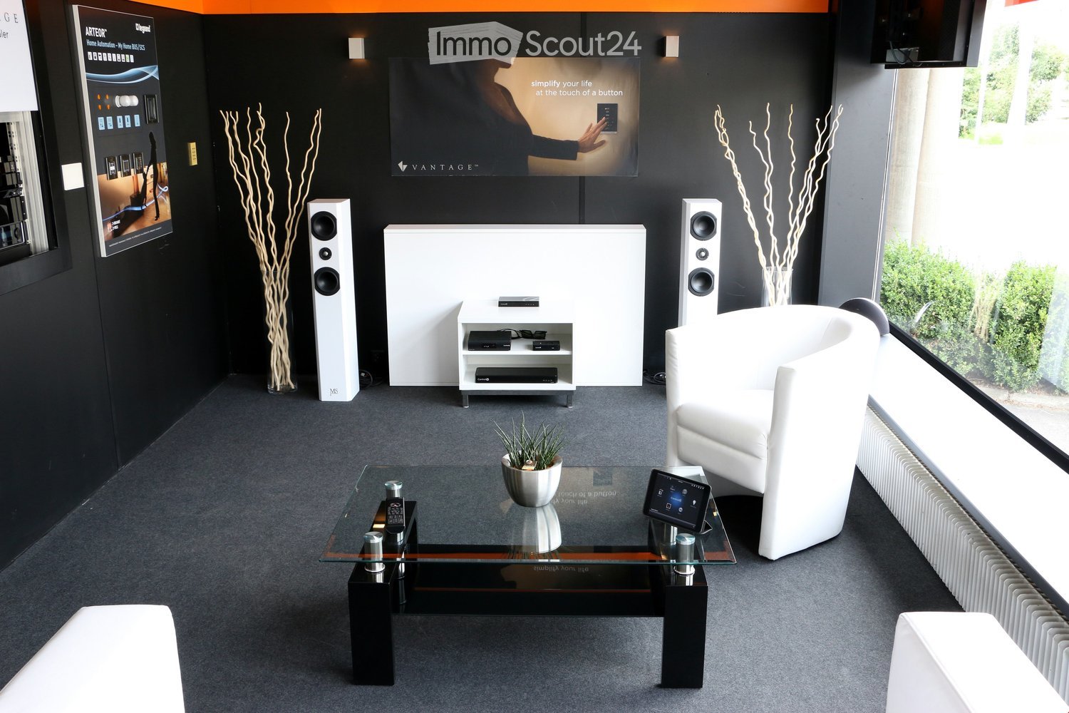 Modern living room with white sofa, glass coffee table, speakers, and decorative vases.