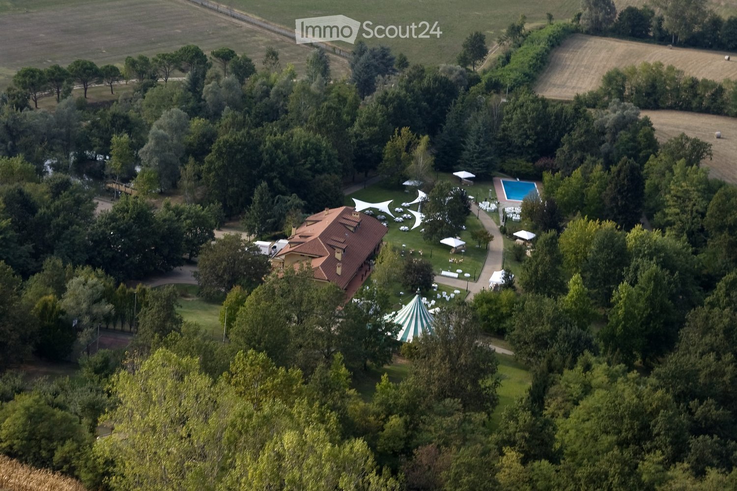 Aerial view of a large estate with a house, swimming pool, outdoor seating area, and surrounding greenery.