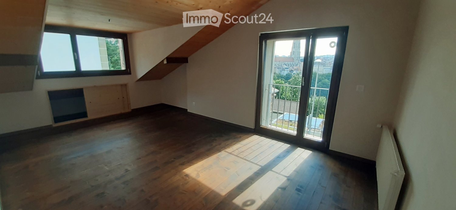 Spacious attic room with wooden beams, large windows, and a balcony/terrace overlooking the city