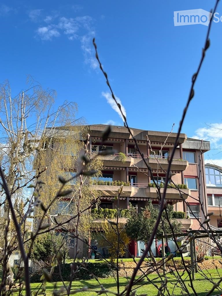 Multi-story residential building with balconies, surrounded by greenery and trees.