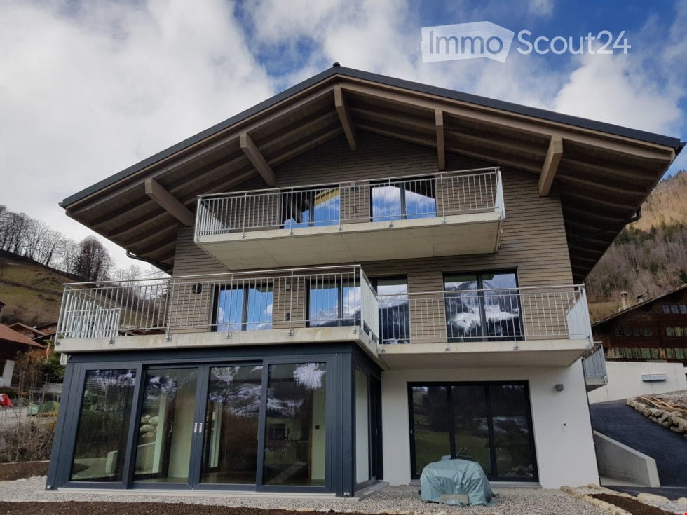 Modern two-story house with large windows, balconies, and a view of the mountains.