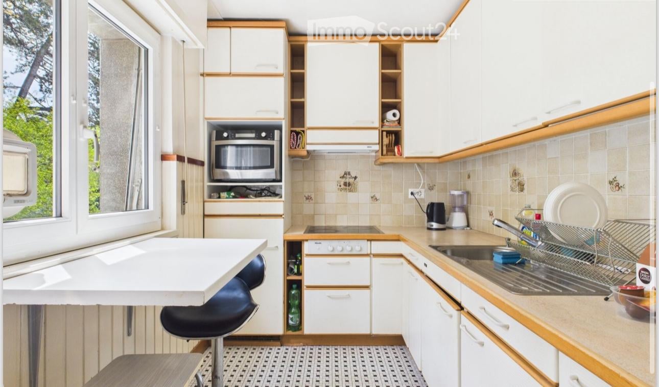 A compact kitchen with white cabinets, a microwave, a sink, a blender, and a small table with a chair.