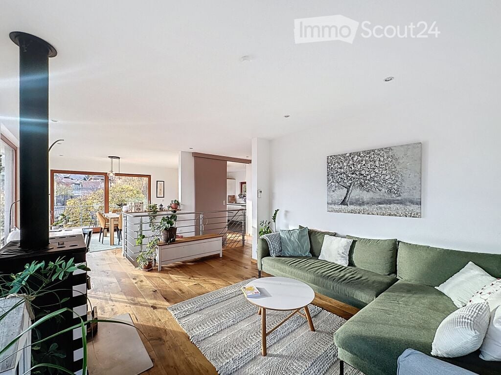 Modern living room with a green sectional sofa, white coffee table, fireplace, artwork, and large windows.