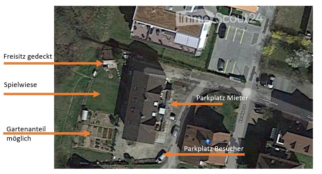 Aerial view of a residential area showing a building, parking spaces for tenants and visitors, a covered outdoor seating area, a playground, and a possible garden area.