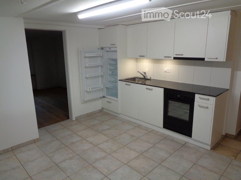 Modern kitchen with white cabinets, a black countertop, a stainless steel sink, and an open refrigerator. The floor is tiled, and the walls are painted white.