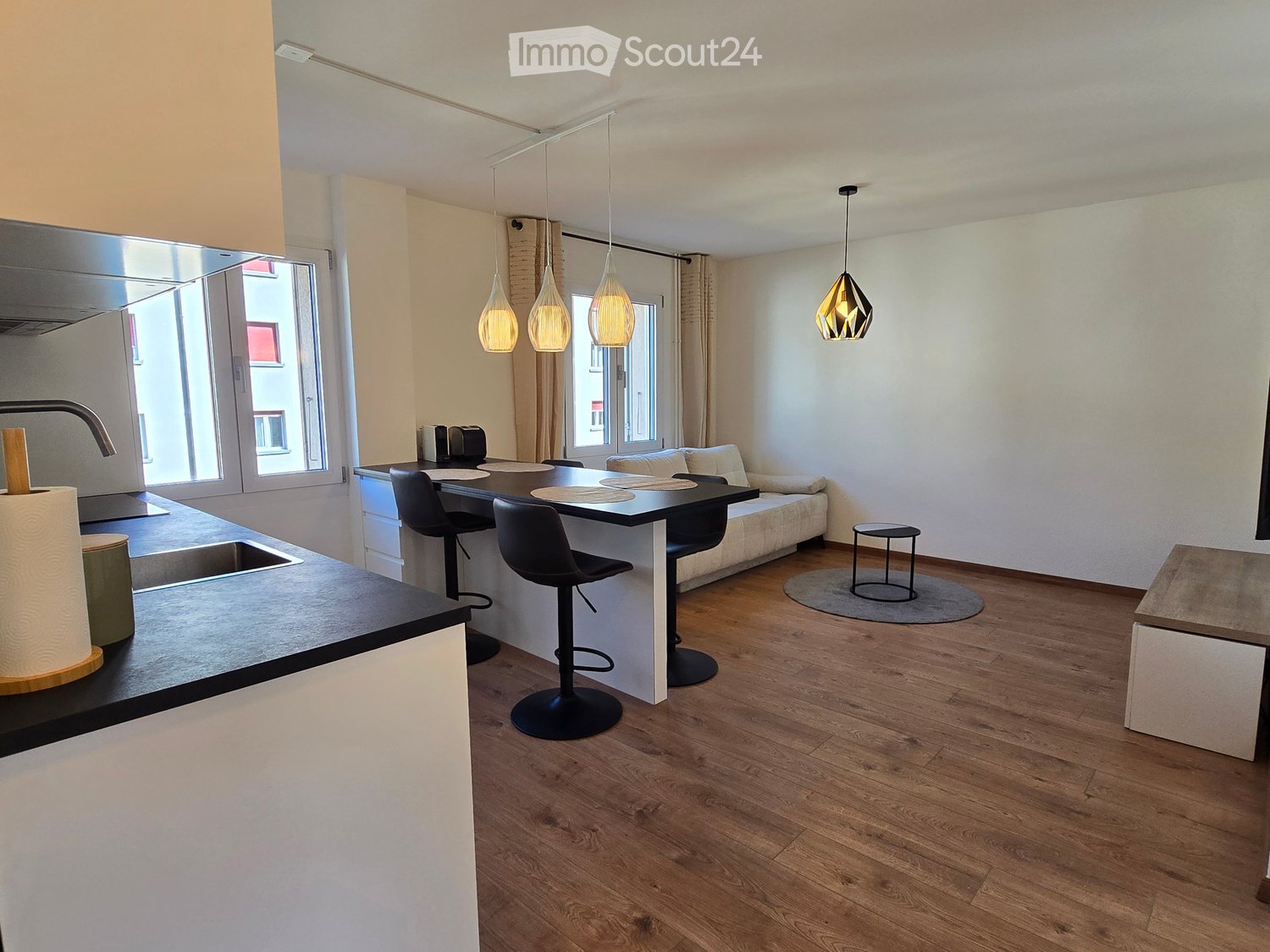 Modern open-plan living and dining area with a sofa, coffee table, dining table, chairs, and a kitchen island with a sink and faucet.