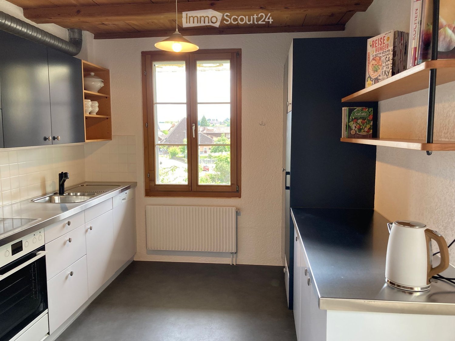 Kitchen. Modern kitchen with white cabinets, stainless steel sink, built-in oven, wooden shelves holding books, and a kettle on the counter.