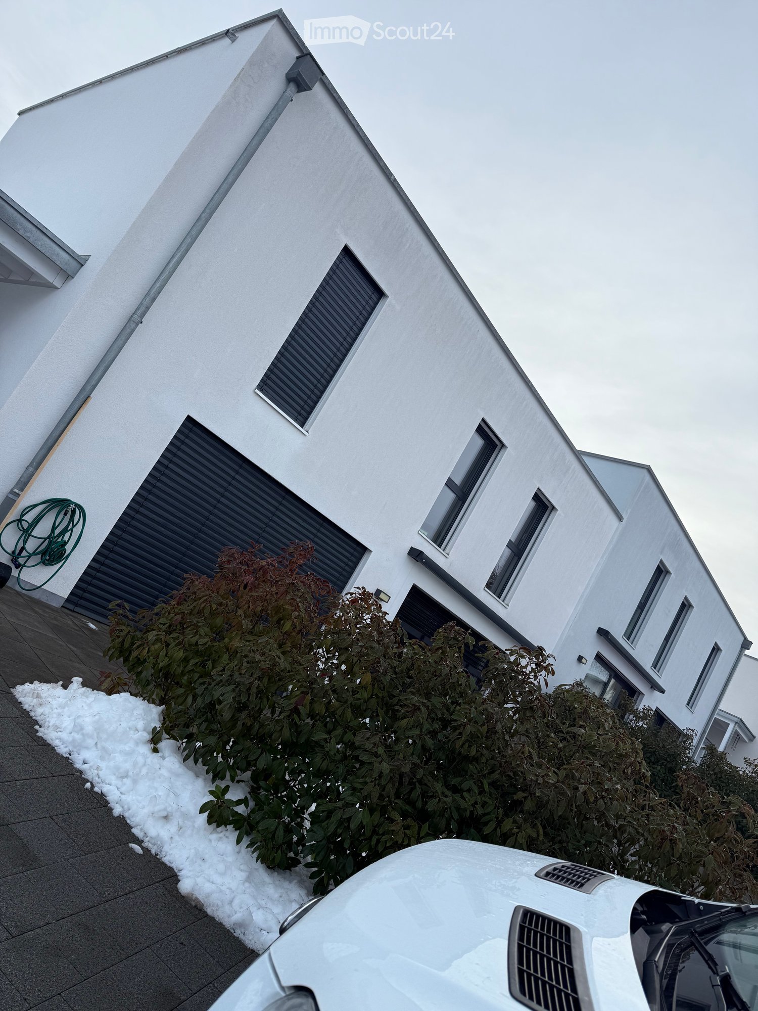Modern two-story house with white exterior, multiple windows, garage, and surrounding greenery.