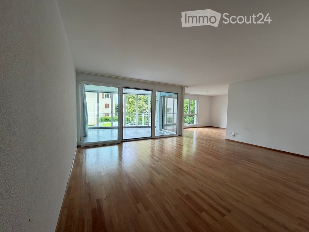 Empty room with wooden flooring, large sliding glass doors leading to a balcony, and white walls.
