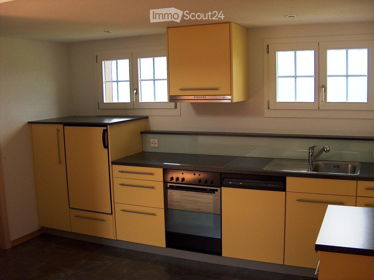 Modern kitchen with light yellow cabinets, black countertops, and stainless steel appliances including an oven, dishwasher, and sink.