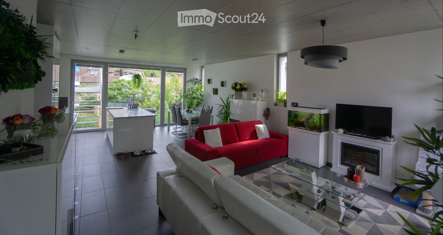 Modern living room with a red sofa, glass coffee table, fireplace, fish tank, and a kitchen island visible in the background.