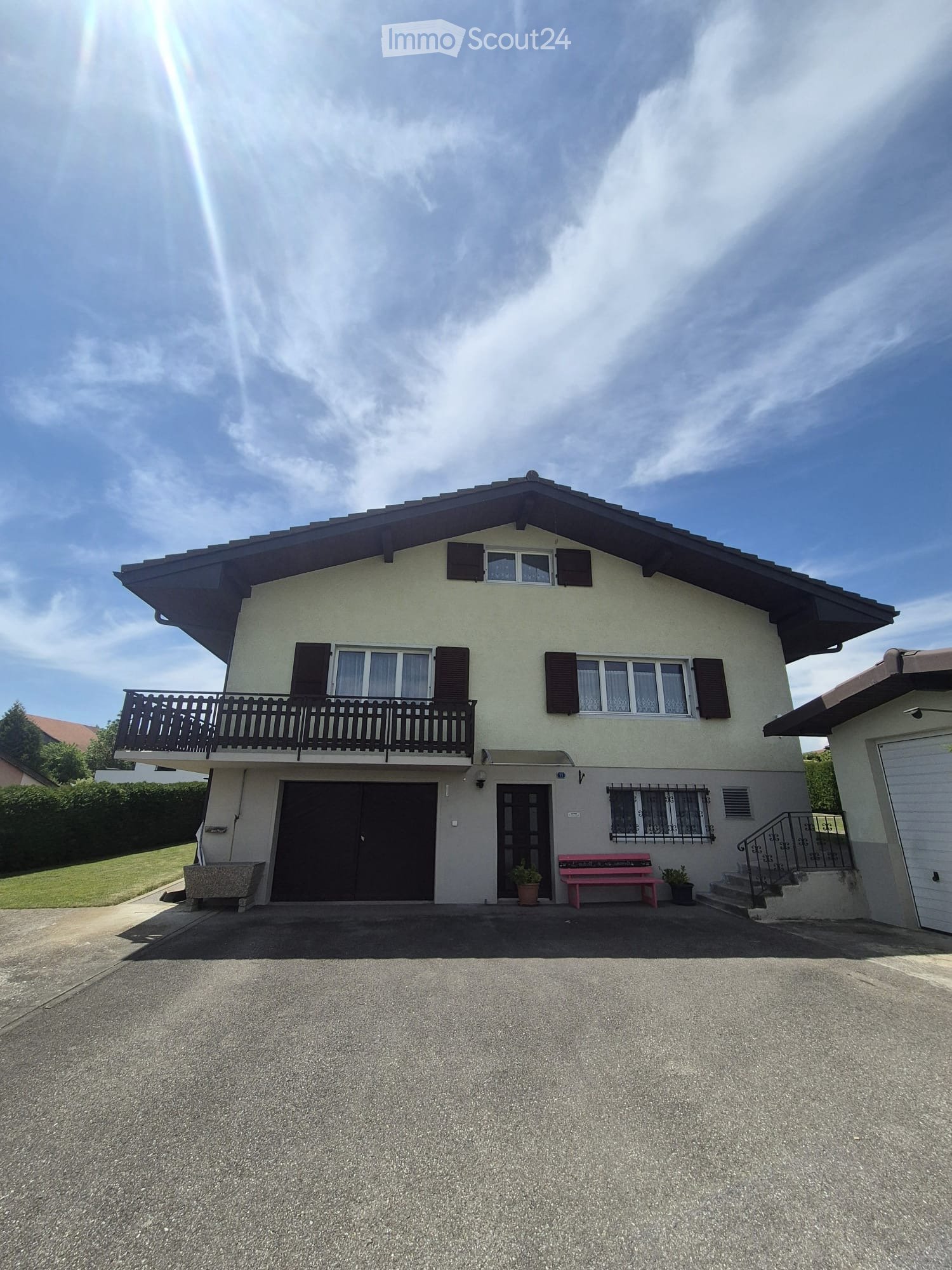 Two-story house with a balcony, garage, and a small garden area with a bench and potted plants.