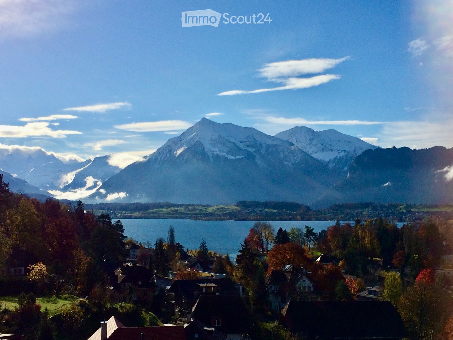A scenic view of a town nestled in a valley with a lake and snow-capped mountains in the background.