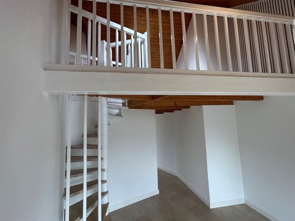 Spiral staircase leading to an upper level with white railings and wooden beams, white walls, and a tiled floor.