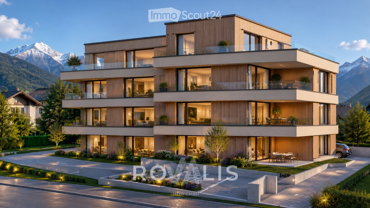Modern multi-story residential building with large glass windows, balconies, and a landscaped garden area. The structure features contemporary design with wooden paneling and is situated in a scenic mountainous region.