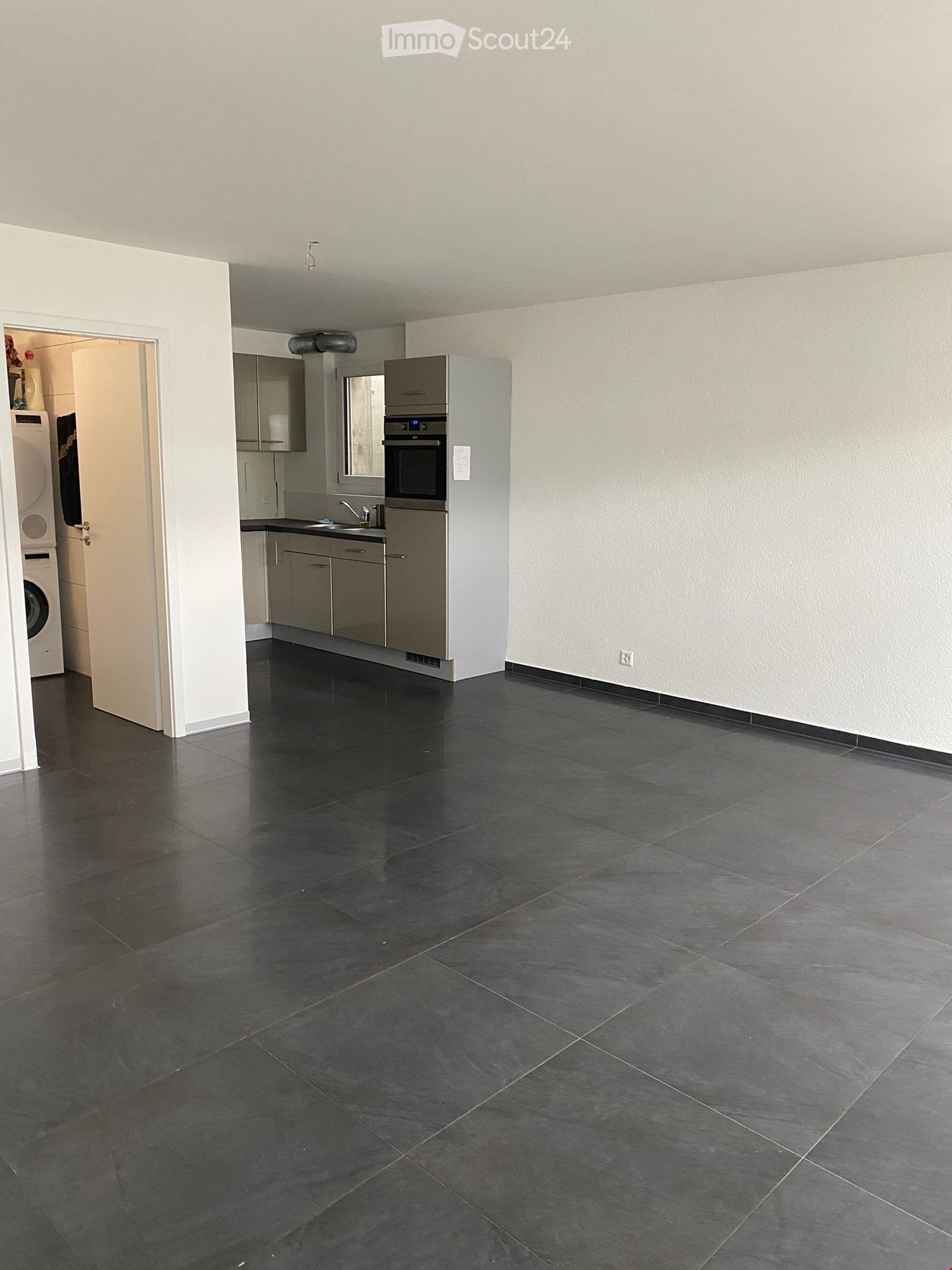 Empty kitchen with dark tiled floor, grey cabinets, and stainless steel appliances including an oven and sink.