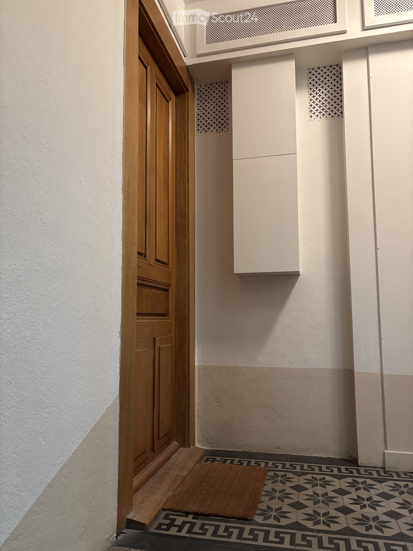 Hallway with patterned tile floor, white walls, wooden door frame, and a small doormat.