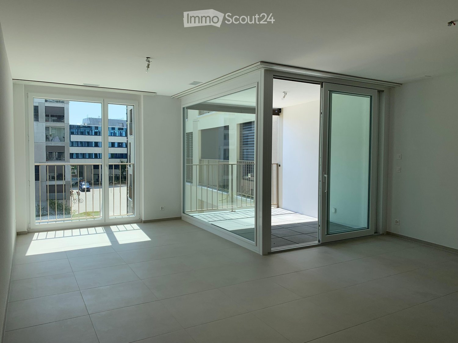 Empty room with tiled floor, large sliding glass doors leading to a balcony, and a view of a modern building outside.