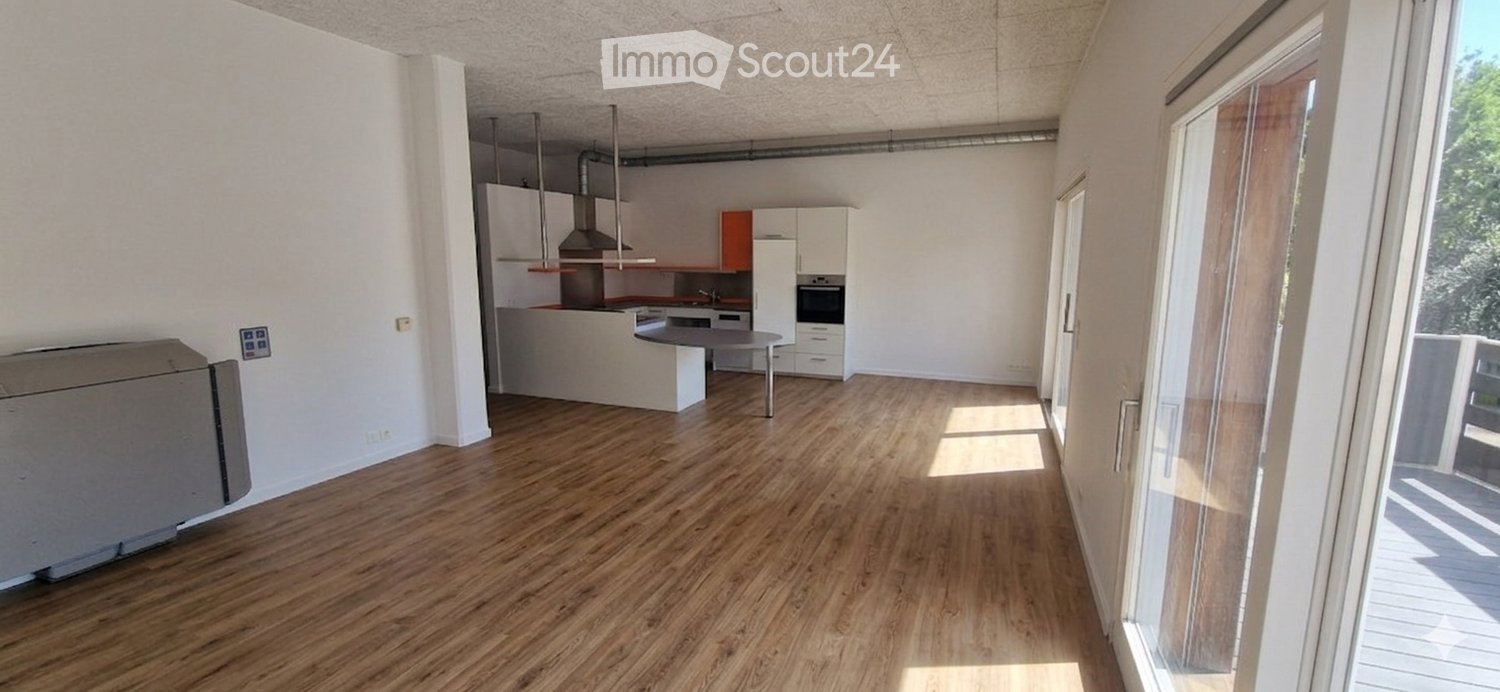 Open-plan living and kitchen area with wooden flooring, white kitchen units, and a large window leading to a balcony.