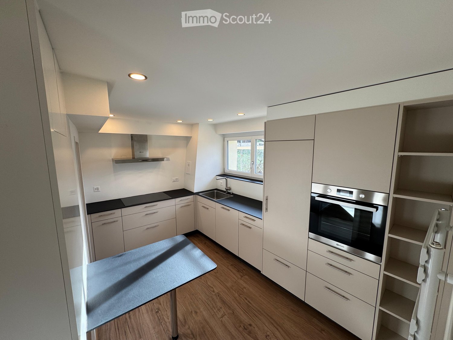Modern kitchen with white cabinets, stainless steel oven, sink, and a small table with a blue cloth.