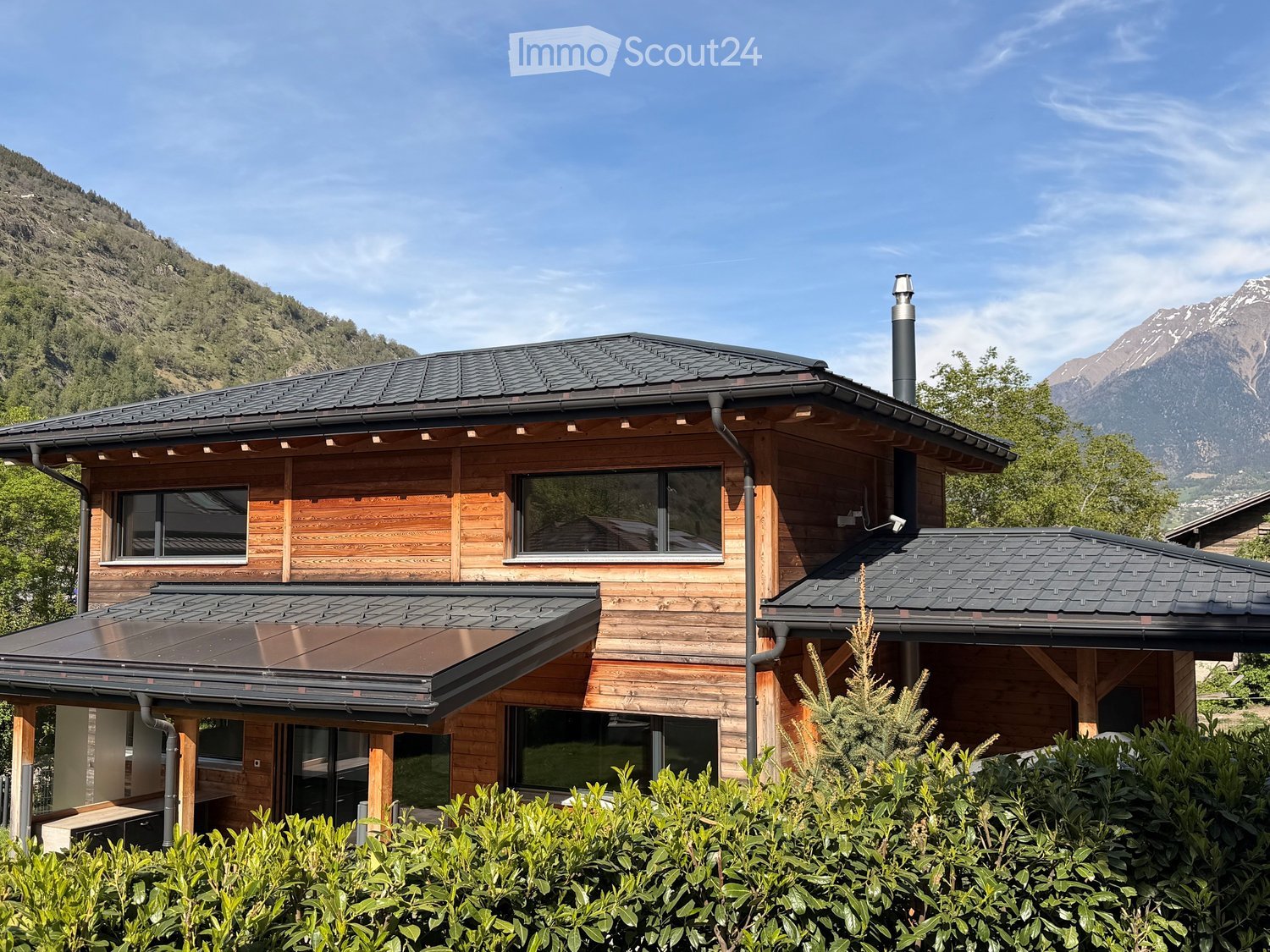 wooden exterior, black roof, solar panels, large windows, mountains in the background