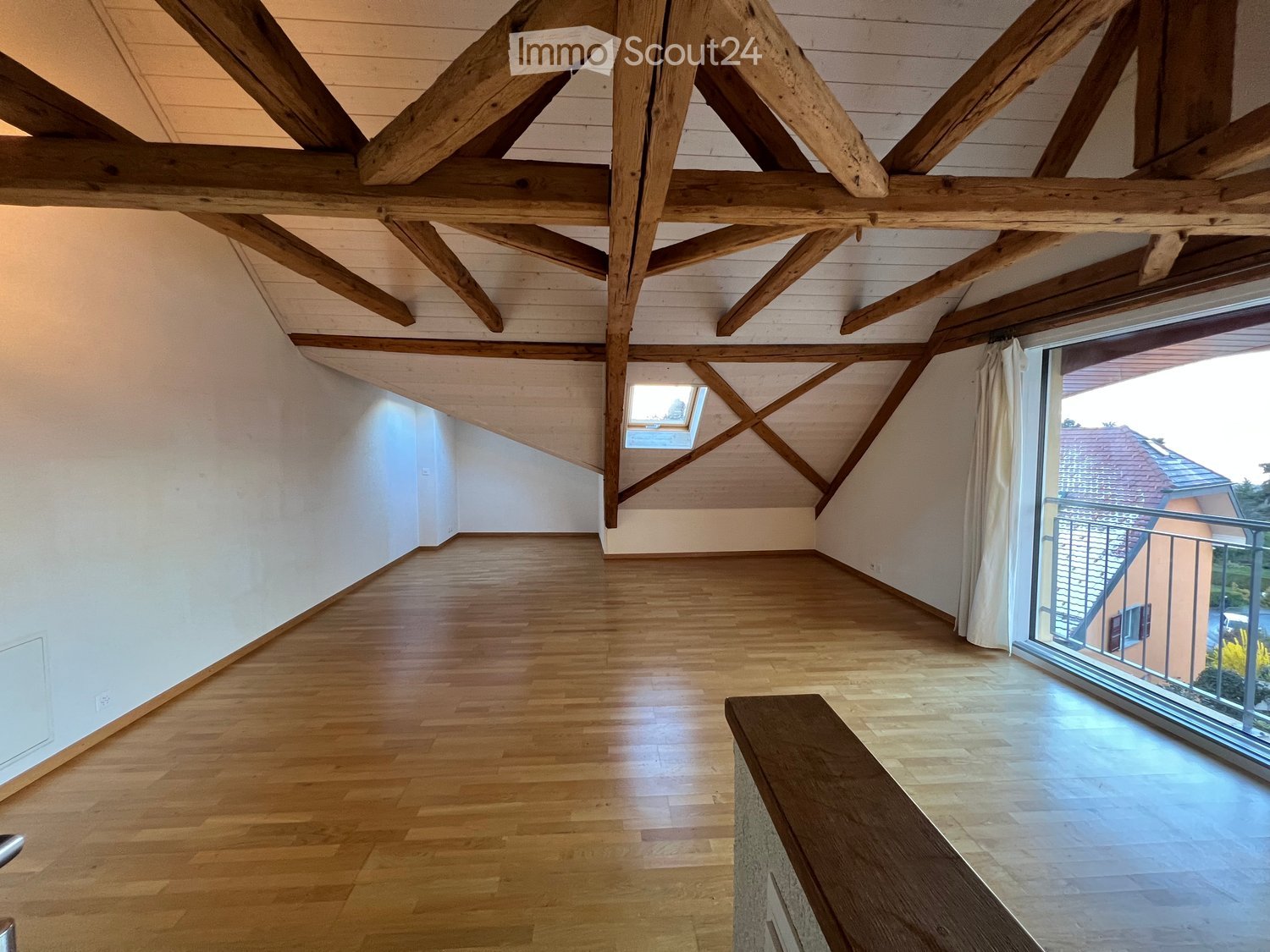 Empty attic room with wooden beams, wooden flooring, large window, and skylight.