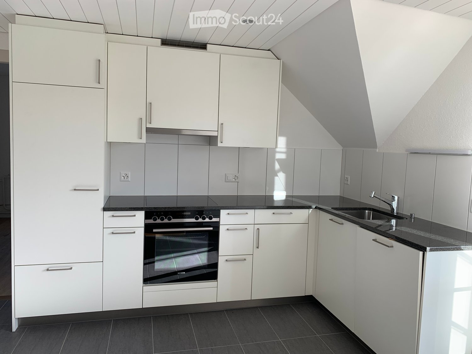 Modern kitchen with white cabinets, black countertops, and stainless steel appliances including an oven and sink.