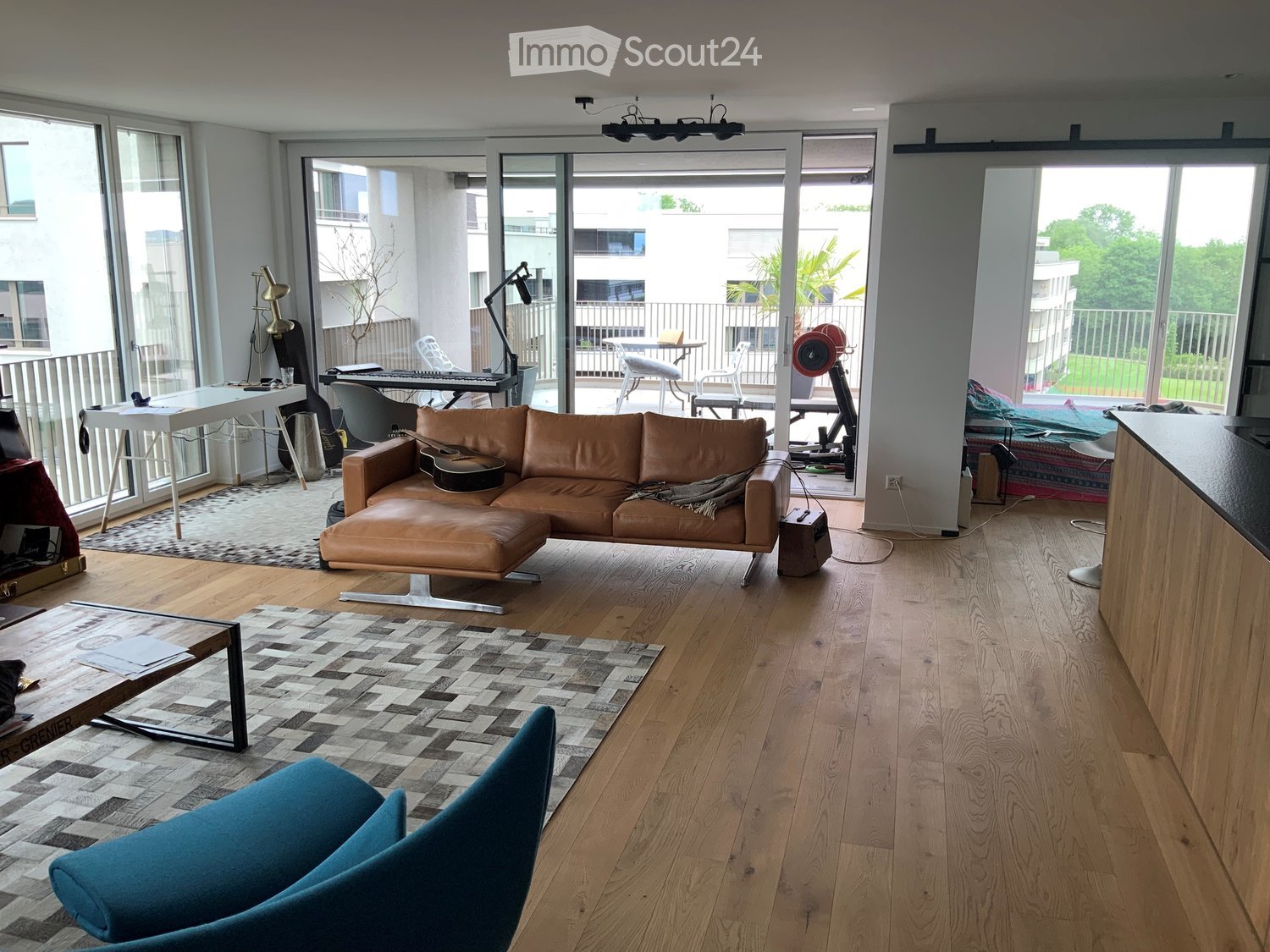open plan living space, modern decor, hardwood floors, large windows, balcony with outdoor furniture, comfortable sofa, coffee table, carpet, and artwork on walls
