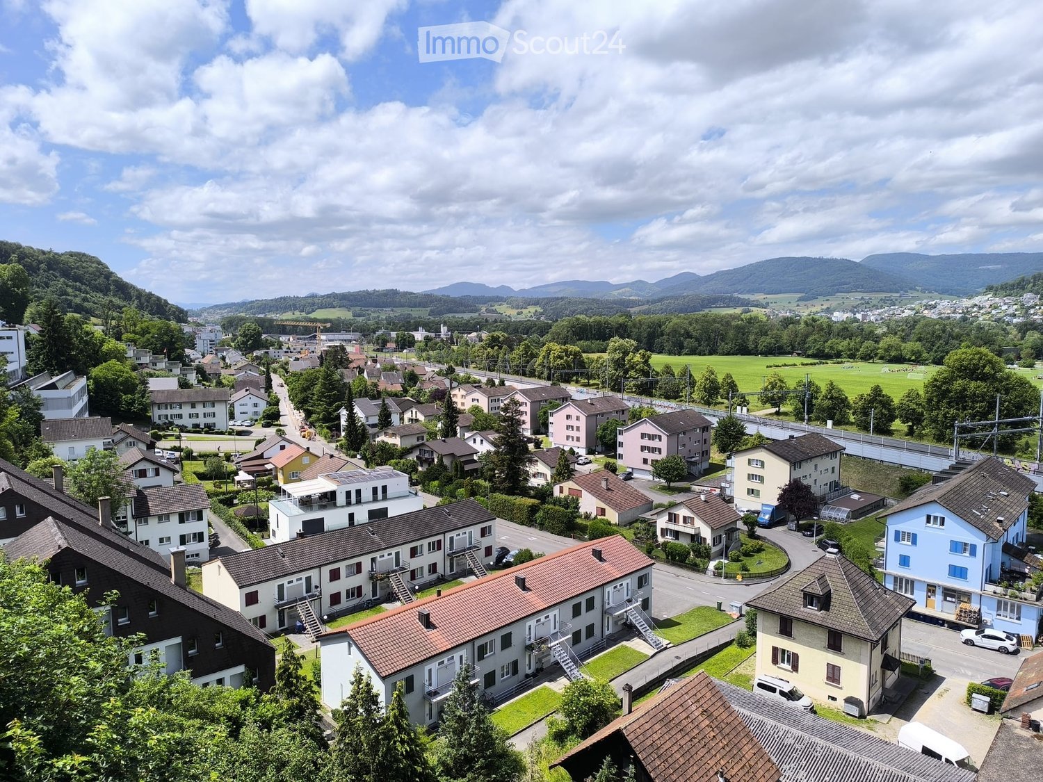 Aerial view of a residential neighborhood with multiple houses, surrounded by greenery and distant mountains.