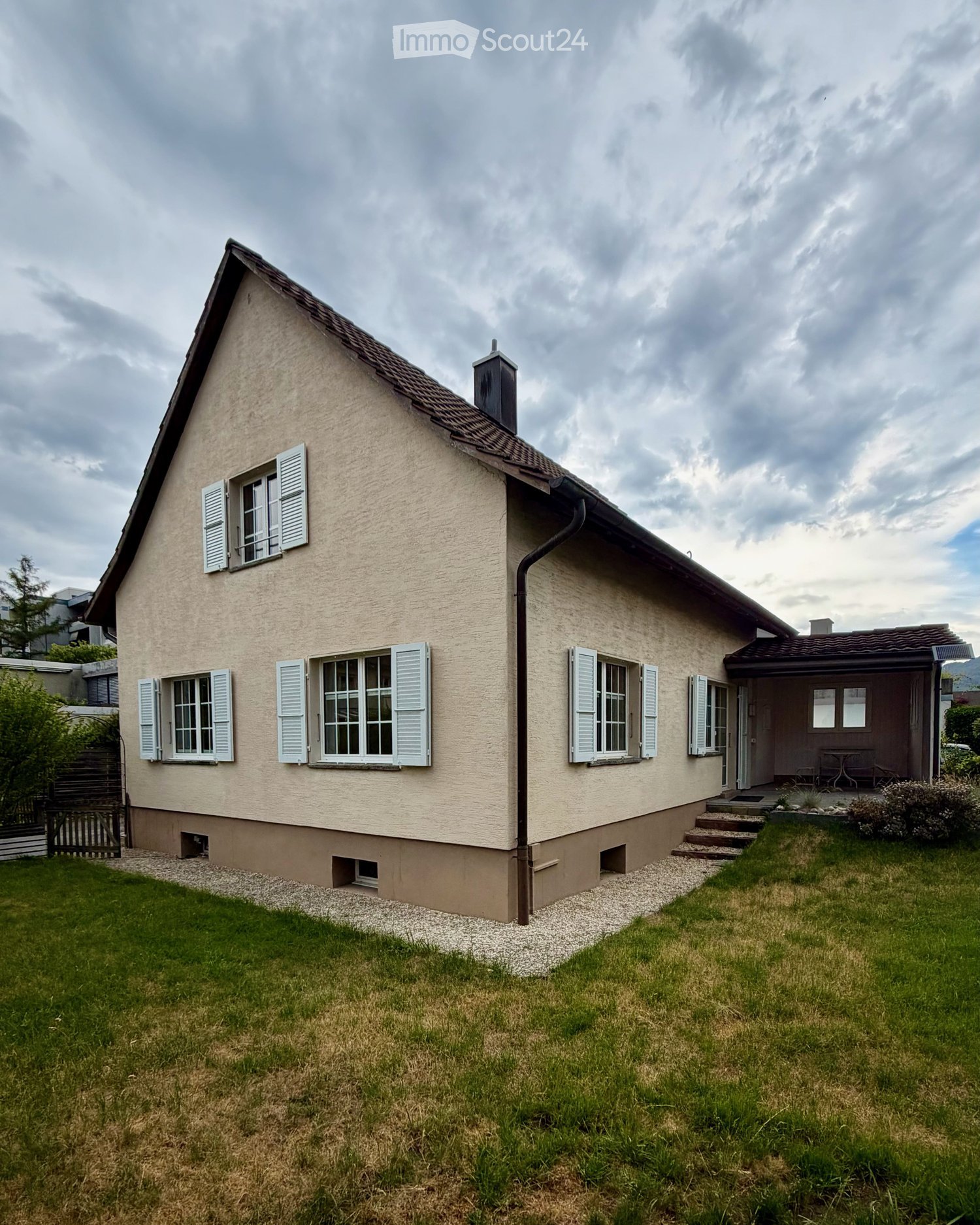 Two-story house with beige siding, white shutters, and a small porch with a table and chairs.