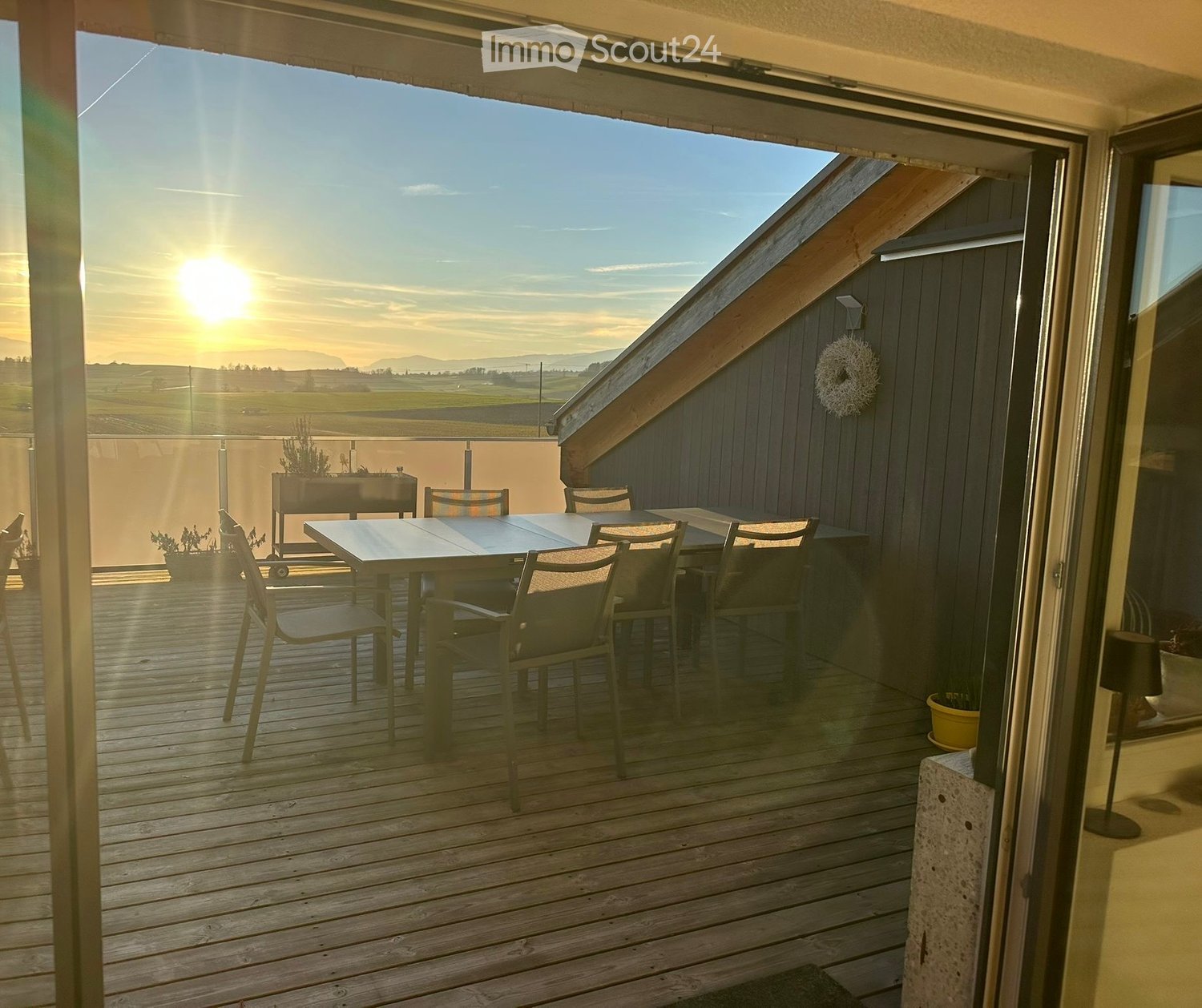 Wooden deck with a table and chairs, overlooking a scenic landscape at sunset.