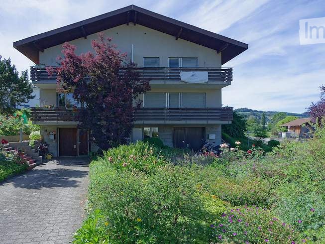 Two-story house with a balcony, surrounded by a well-maintained garden and greenery.
