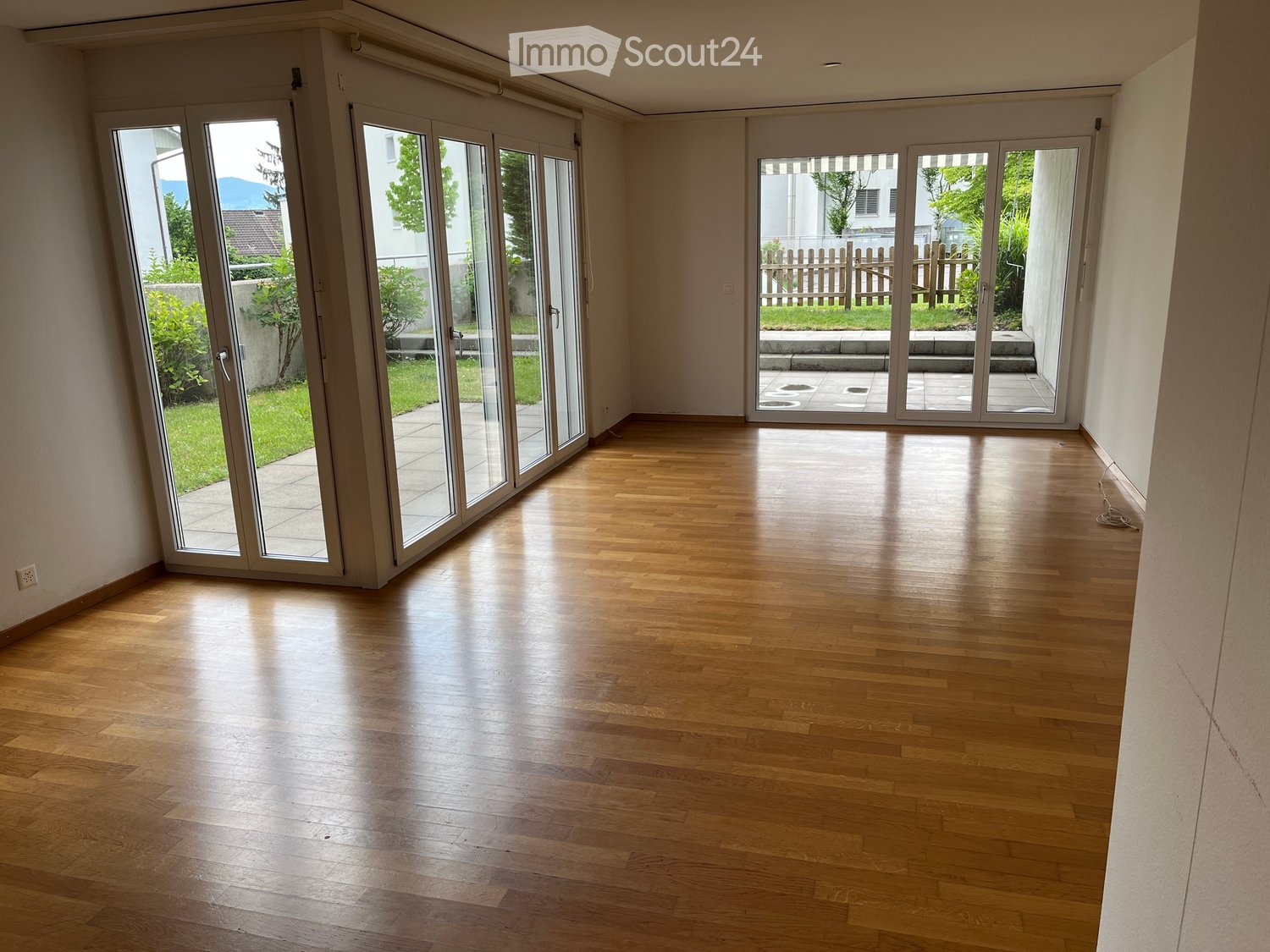 Empty room with wooden flooring and large sliding glass doors leading to a patio and garden area.