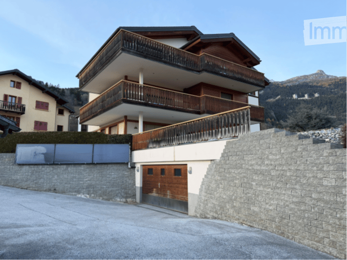 A multi-story wooden and stone house with balconies and a garage, situated in a mountainous area.