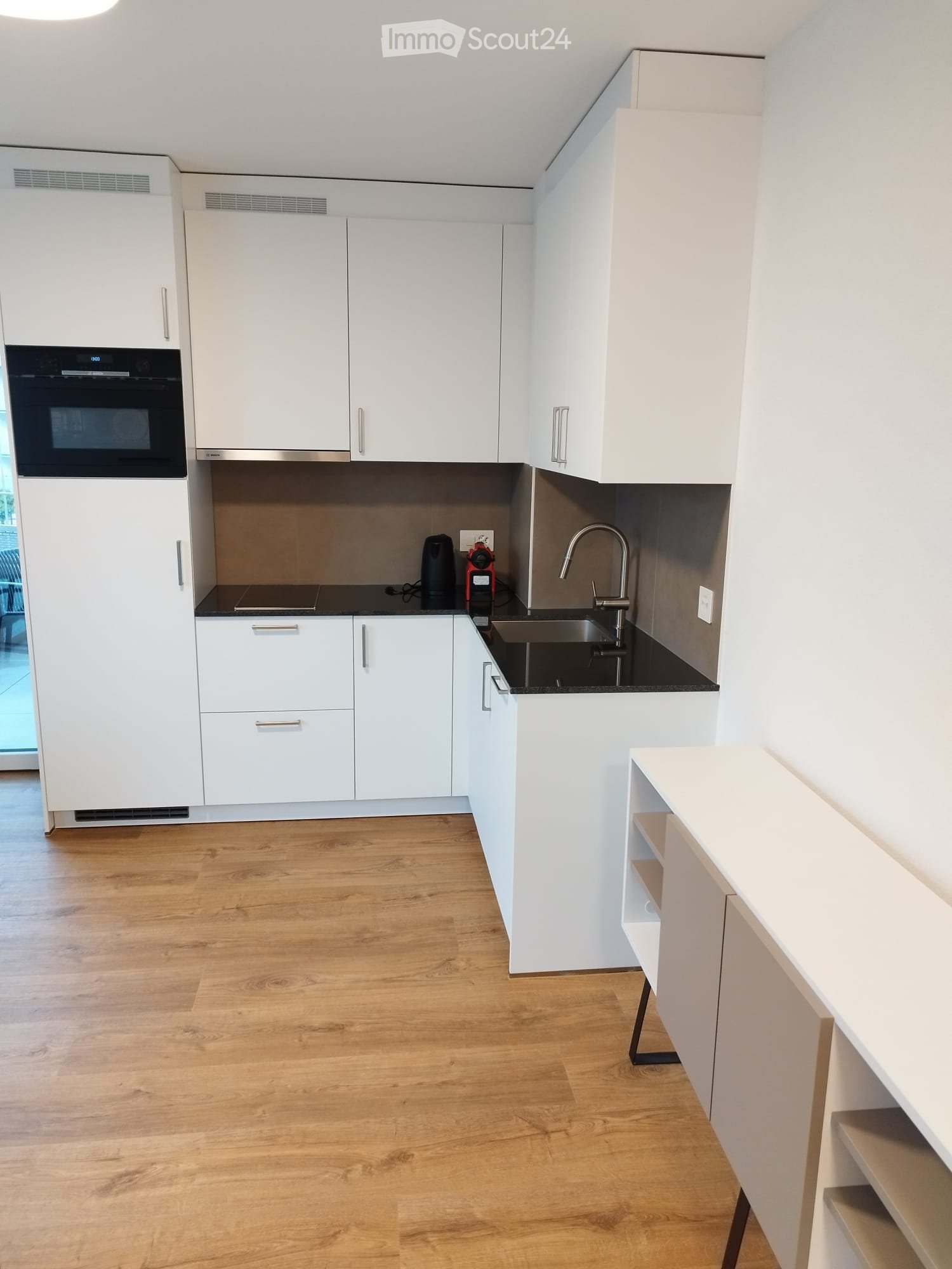 Modern kitchen with white cabinets, wooden flooring, stainless steel sink, and coffee maker on the counter.