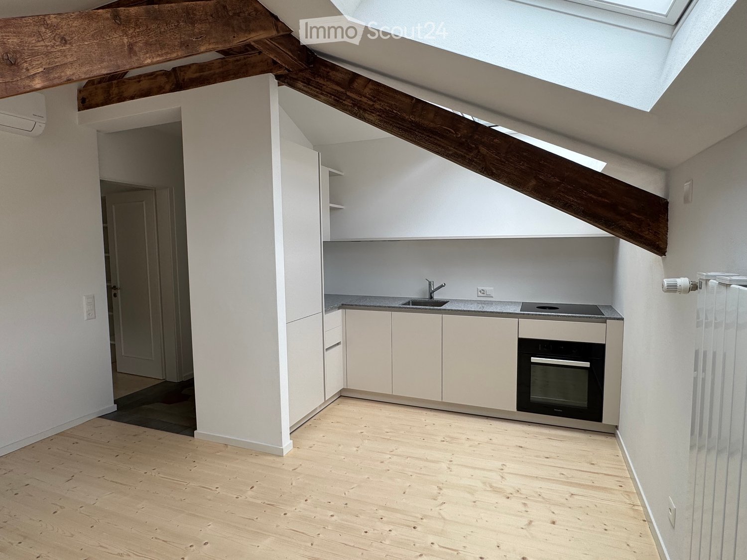 Modern kitchen with light-colored cabinets, a sink, a faucet, and an oven. The space features wooden flooring and exposed wooden beams on the ceiling.