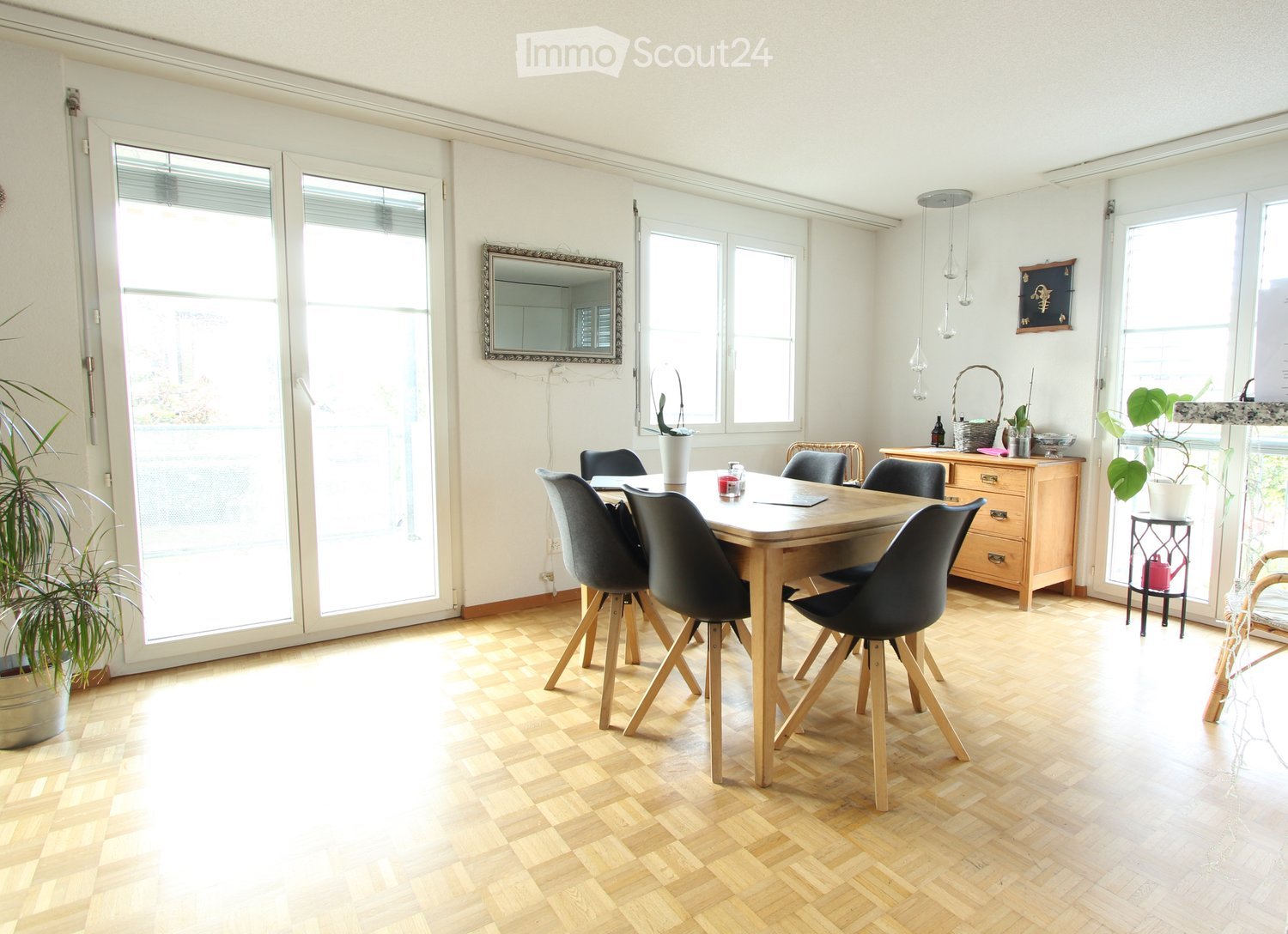 Dining room with wooden table, black chairs, wooden cabinet, plants, and large windows