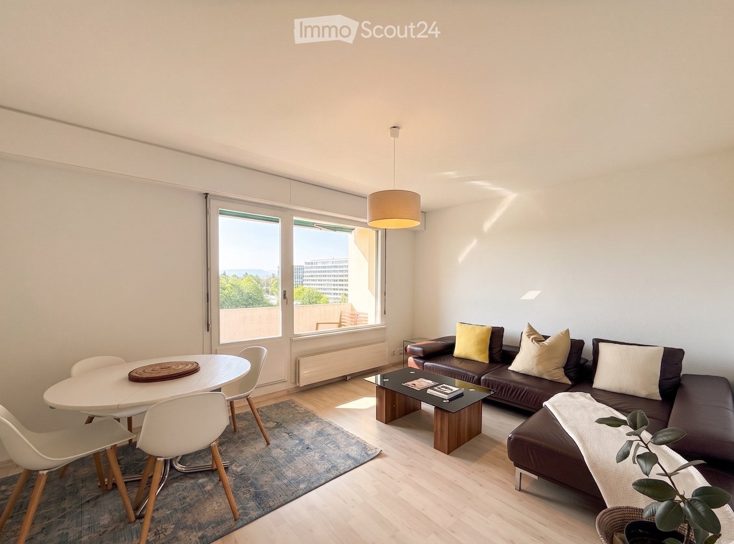 Modern living room with a dark leather sofa, coffee table, dining table with chairs, pendant light, and a view through large windows.