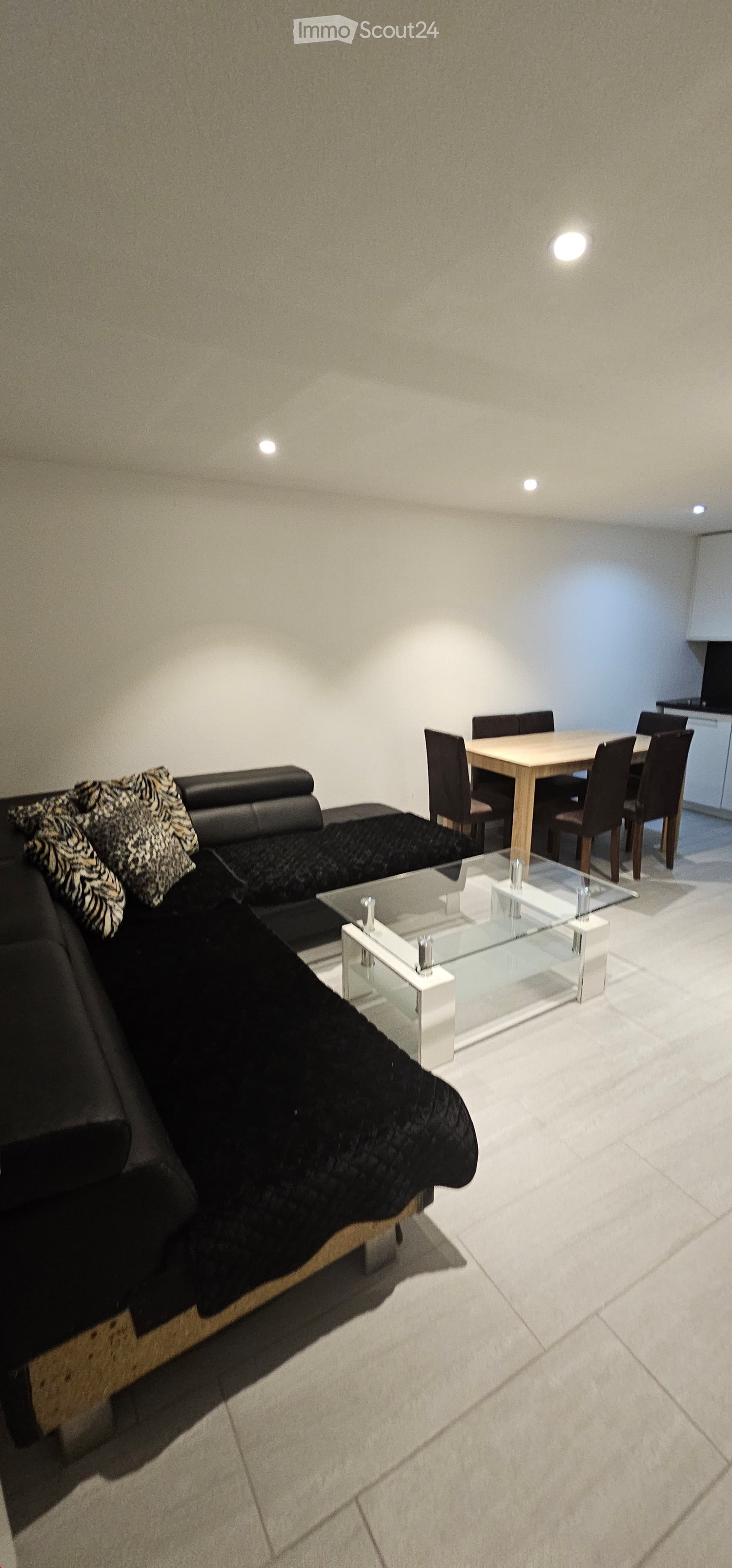 Modern living and dining area with a black leather sofa, glass coffee table, wooden dining table, and chairs.