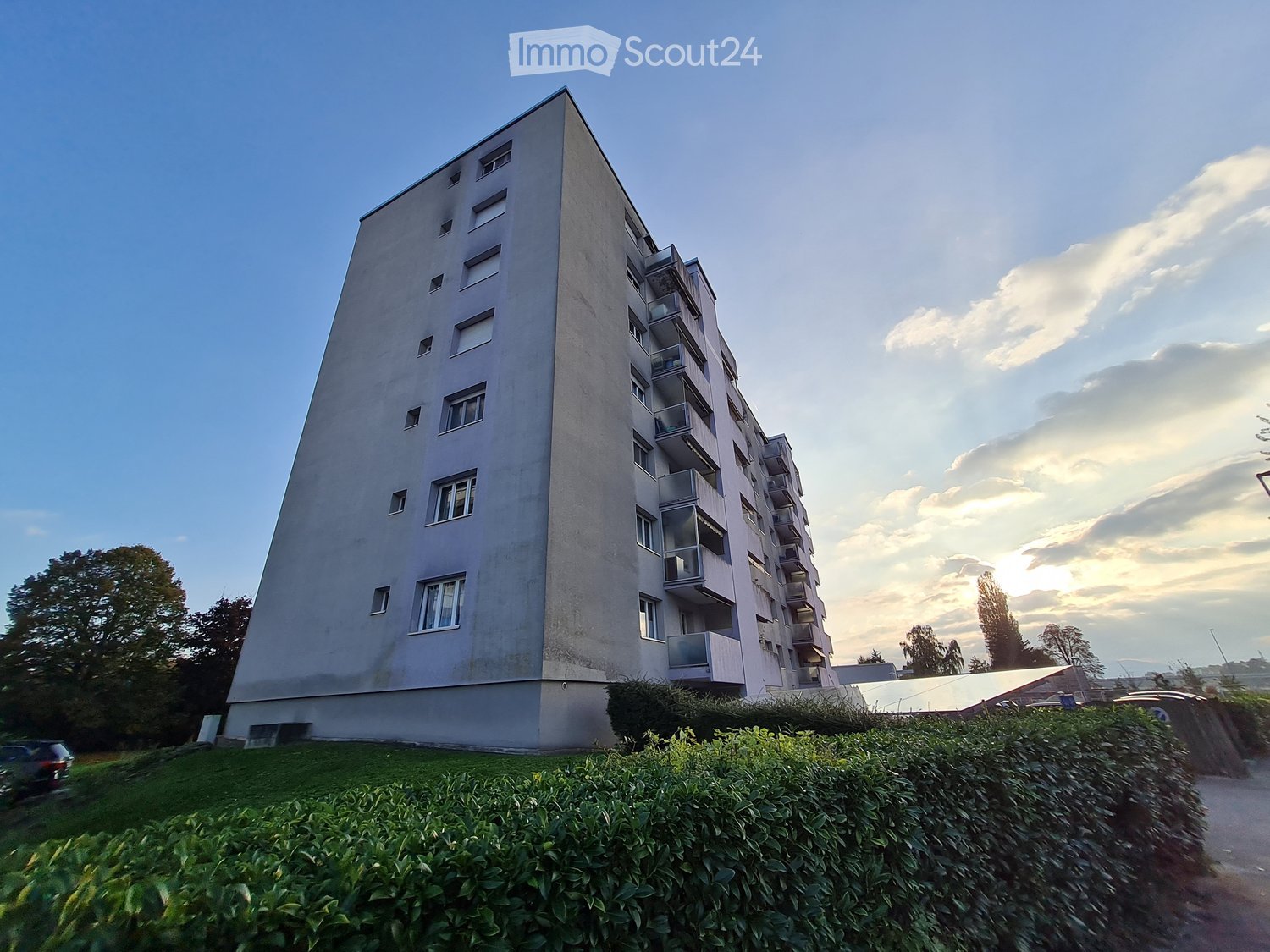 multi story building, balconies, many windows, beige exterior, green hedge, solar panels