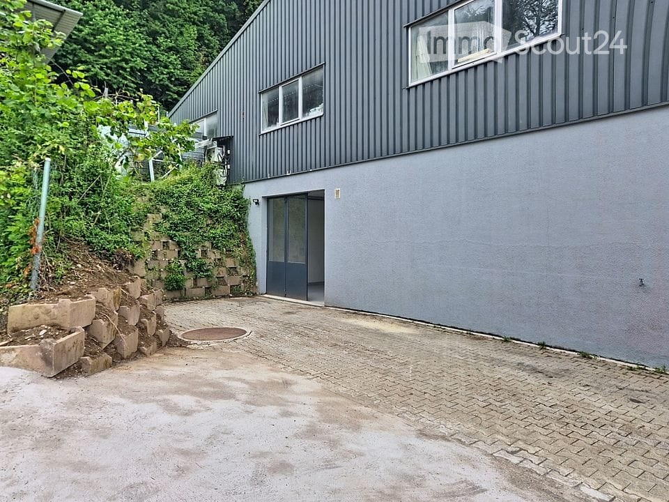 Modern two-story building with grey exterior, raised ground floor, and a paved driveway.