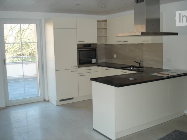 Modern kitchen with white cabinets, black countertops, built-in oven, and stainless steel range hood.