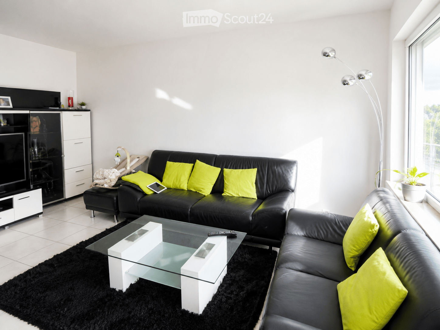 Modern living room with black leather sofas, bright yellow cushions, a glass coffee table, a black shag rug, and a sleek TV stand.