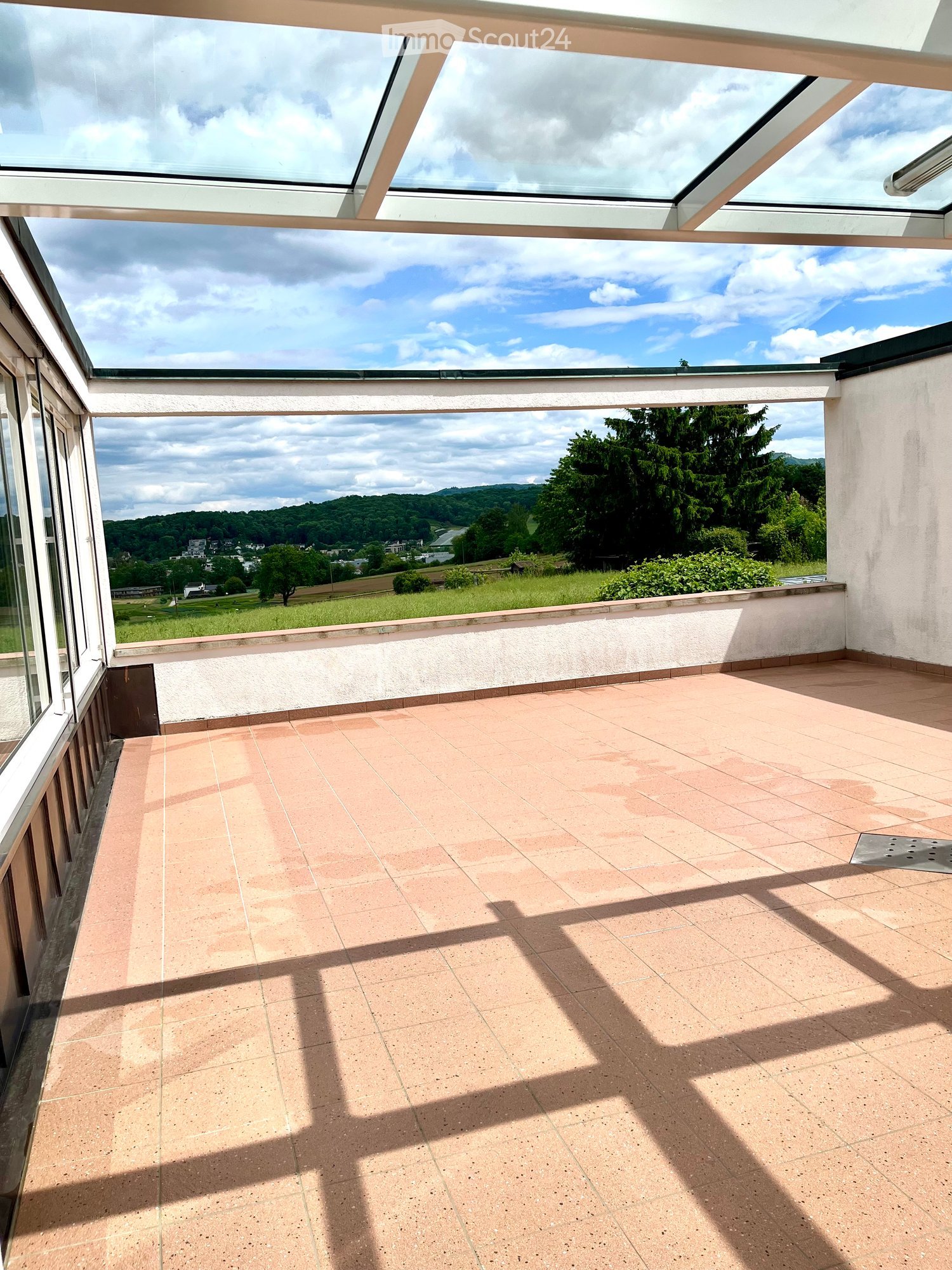 Empty balcony with tiled floor, large glass roof sections, and scenic countryside view.