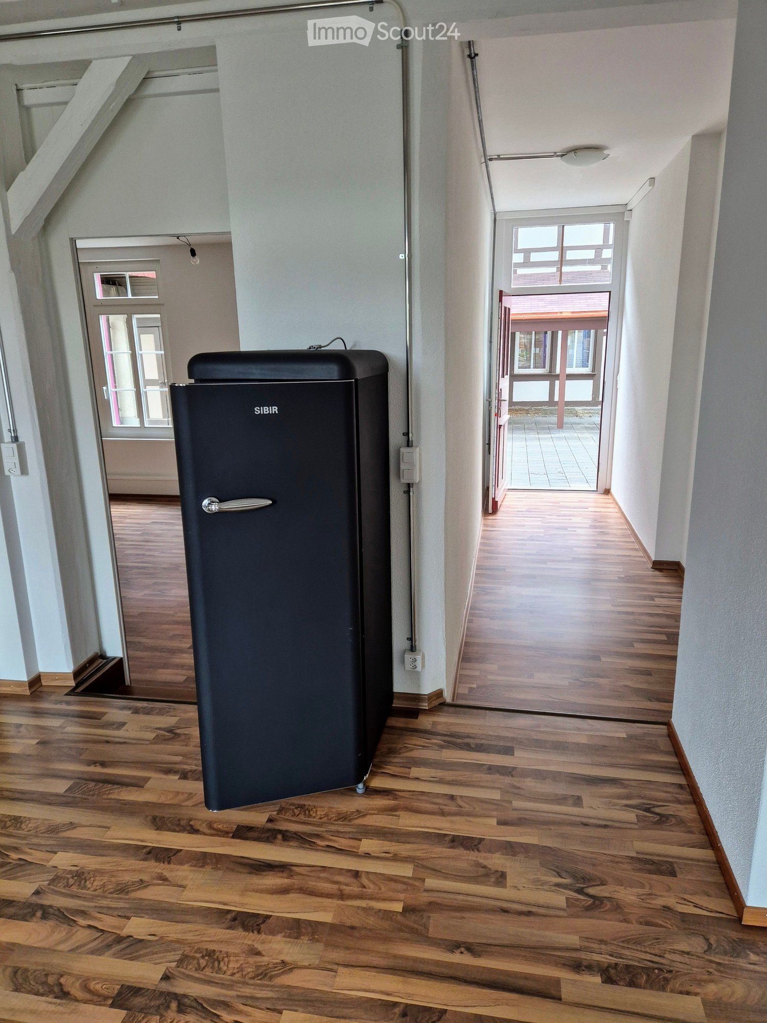 Hallway with wooden flooring, a dark blue refrigerator, and doors leading to other rooms.