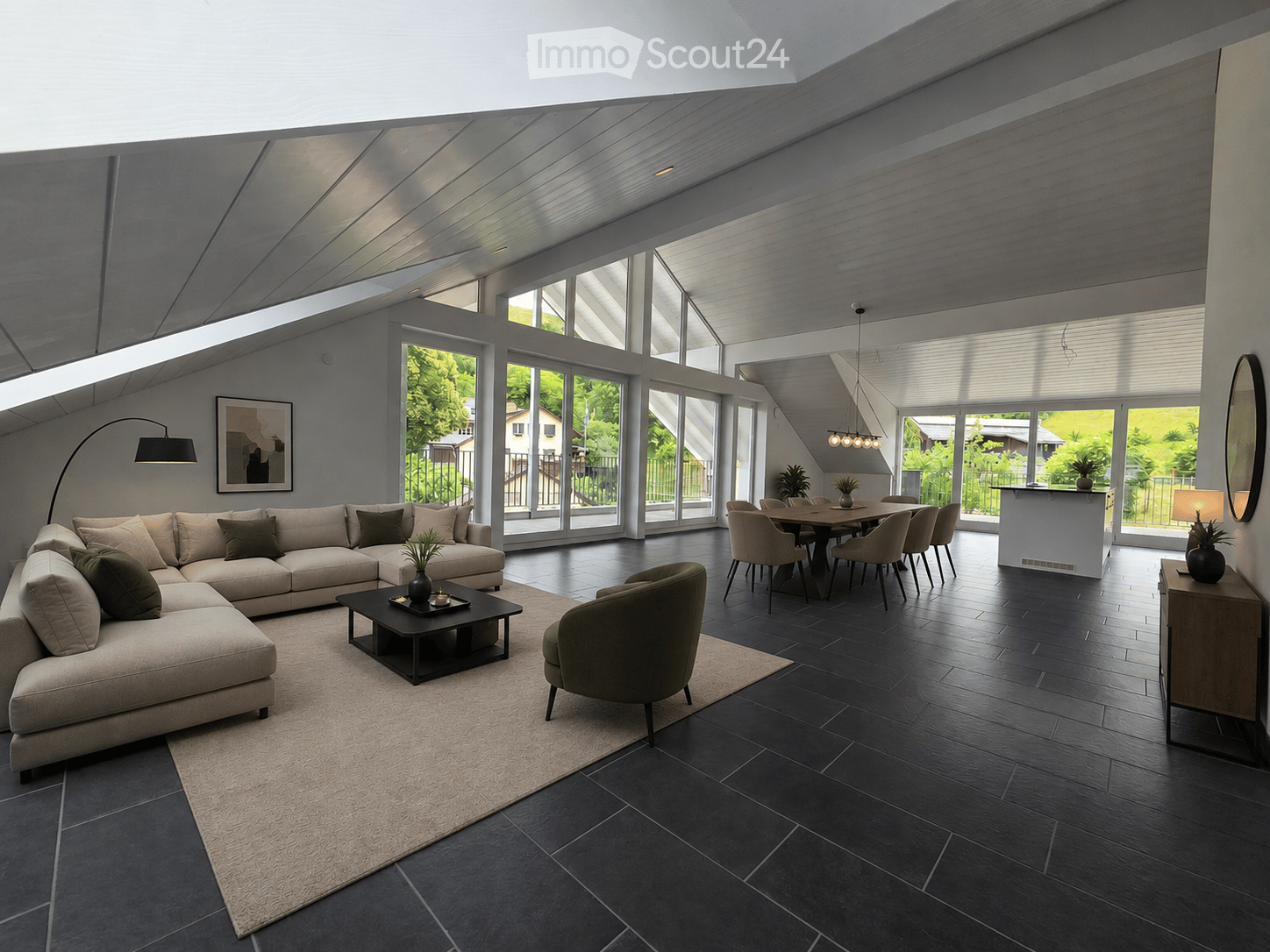Open-concept living and dining area with large windows, dark flooring, a sectional sofa, coffee table, armchair, dining table with chairs, and bar counter.
