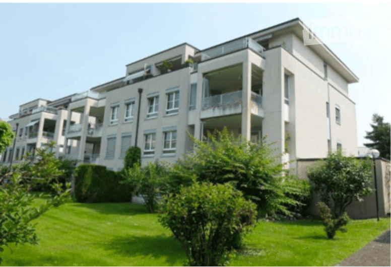 Modern multi-story apartment building with balconies, white facade, and well-maintained green lawn in front.